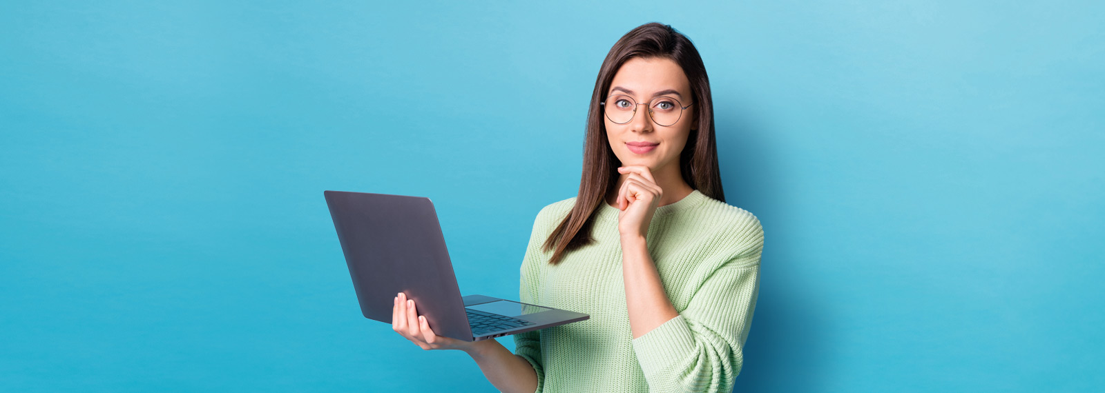 brunette white woman with glasses with yellow sweater holding laptop and hand on chin