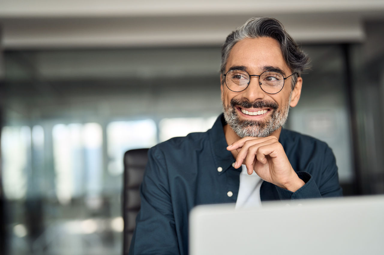 Smiling confident business man sitting at desk using laptop.