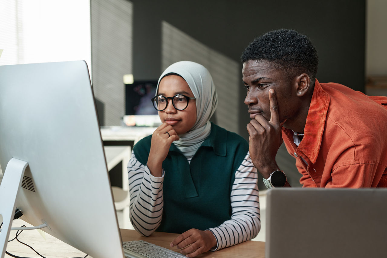 Two young professionals contemplating information shown on a computer screen in an office.