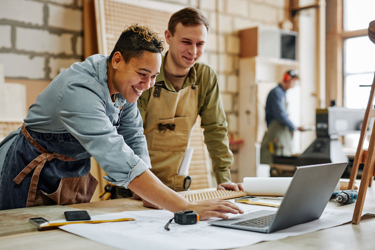 Two small business owners working on laptop in carpentry business shed