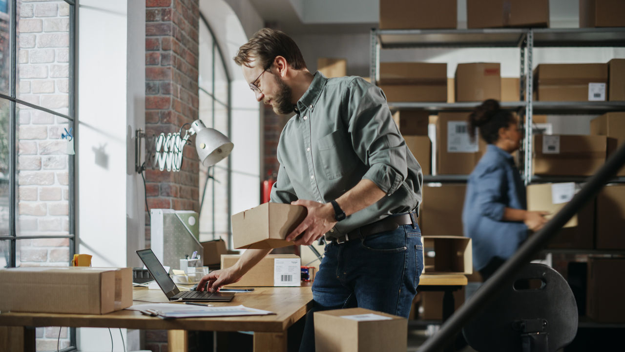 Small business owner looking at contract holding a box in warehouse