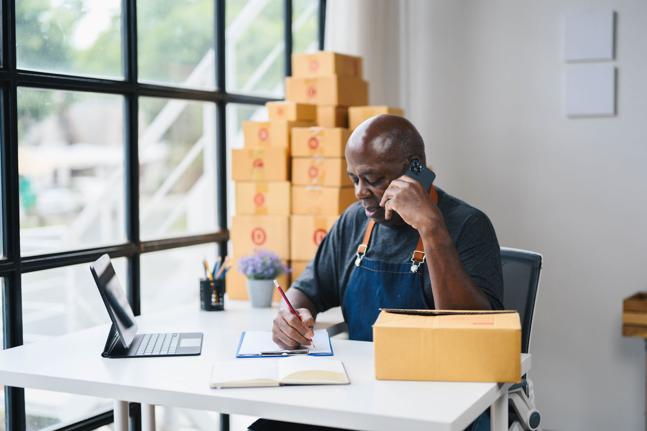 Man managing online business, talking on phone surrounded by cardboard boxes